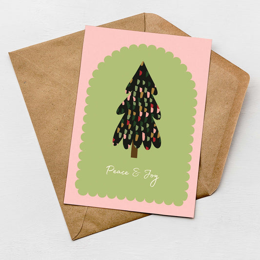 Modern Christmas card featuring a hand-drawn tree illustration with multicolour details on a green and pink background, text reading "Peace & Joy", paired with a kraft envelope.